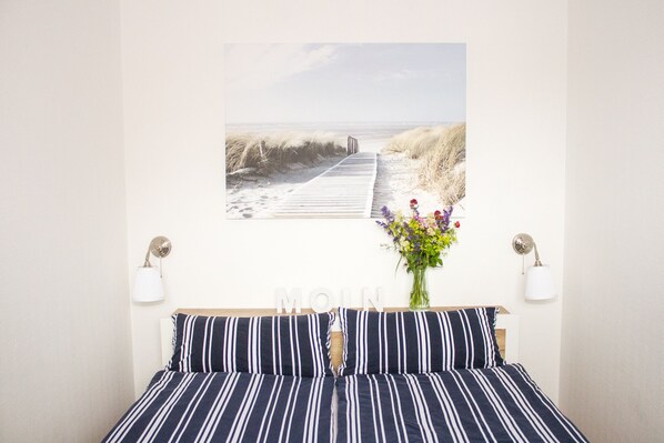 A bedroom with a bed, a wall-mounted artwork of a beach scene, and a vase with flowers.