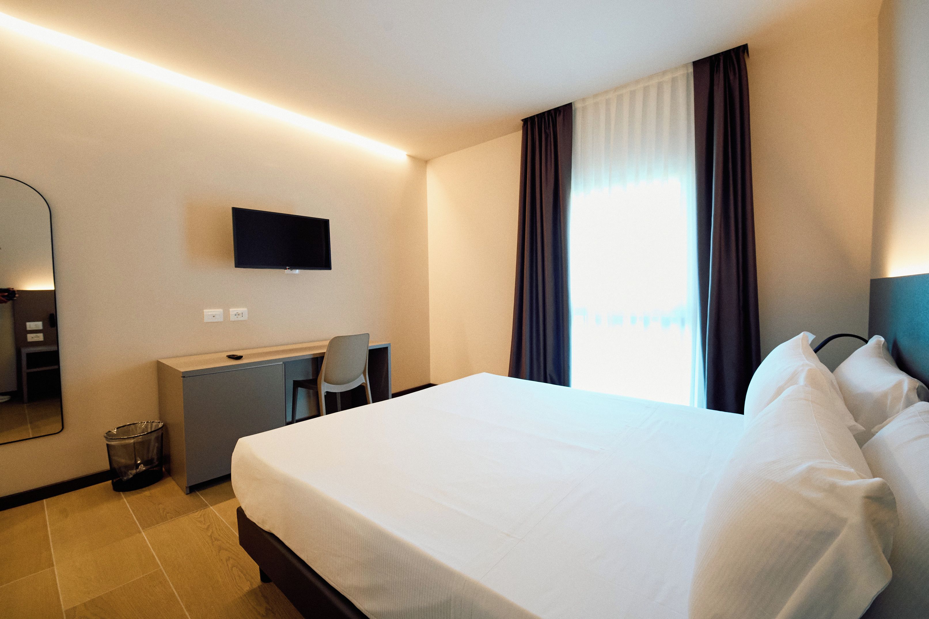Habitación de hotel con cama, escritorio, silla, televisor y ventana con cortinas.