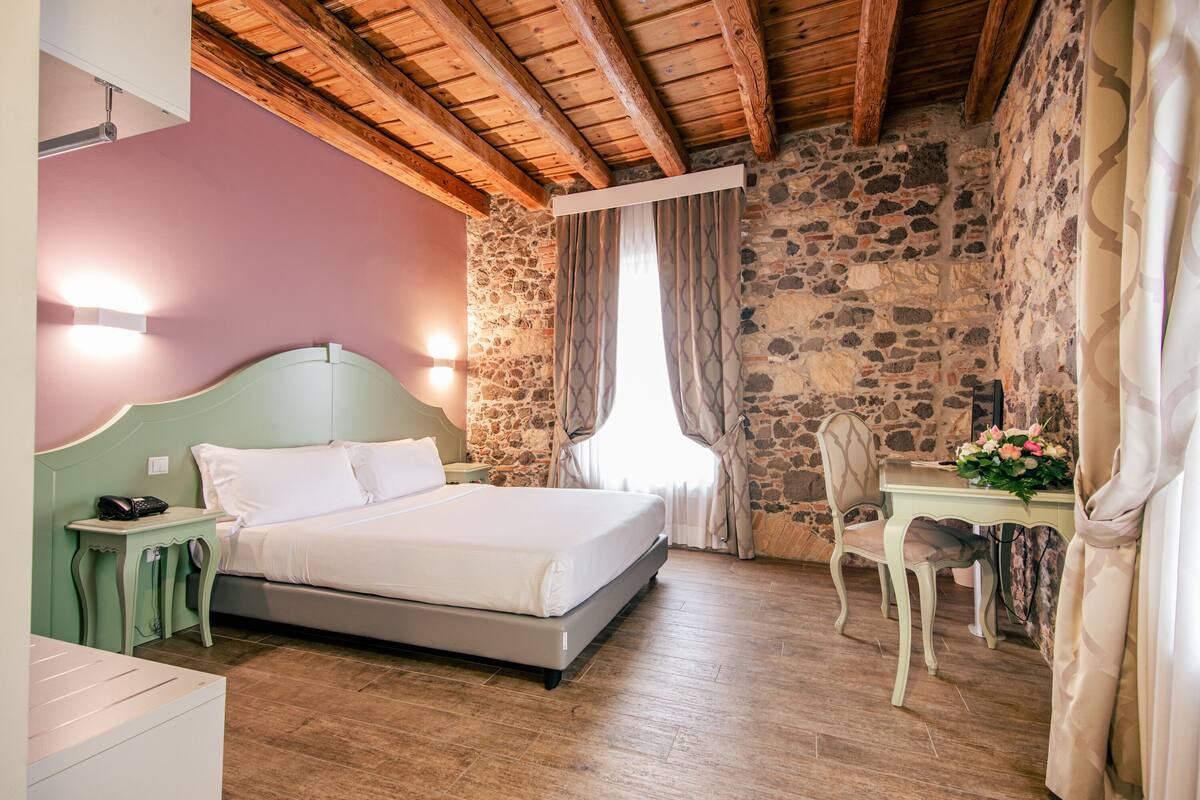 Een slaapkamer met een bed, een nachtkastje, een stoel, een tafel met bloemen en een stenen muur.