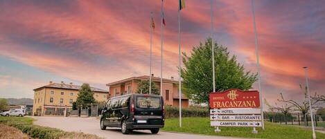 Entrada de un hotel con un cartel de Hotel Fracanzana, una camioneta y banderas.