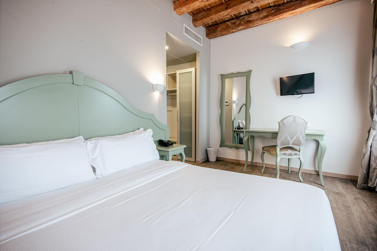 Een slaapkamer met een bed, een bureau, een stoel, een televisie en een spiegel.