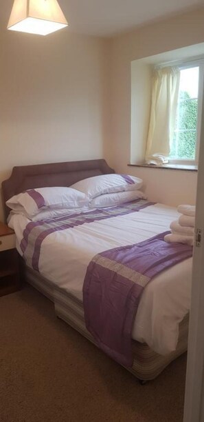 Une chambre à coucher avec un lit, une table de chevet, une fenêtre avec des rideaux et un luminaire au plafond.