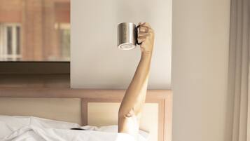 A hand holding a mug above a bed with a wooden headboard.