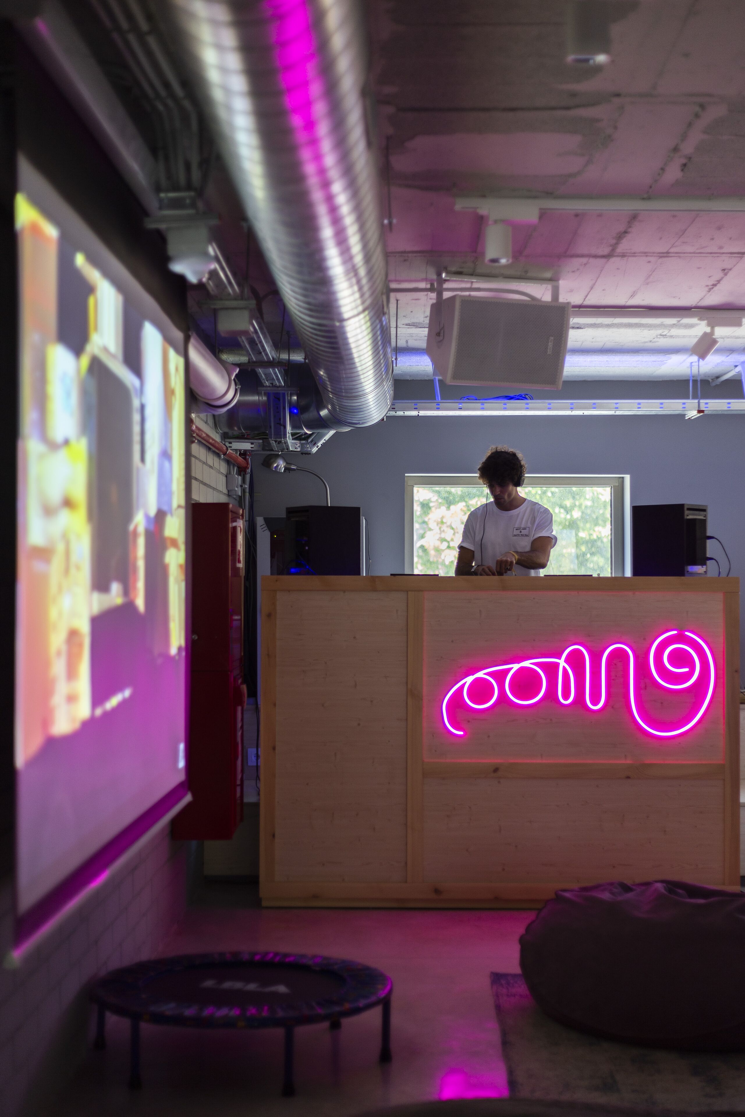A room with a wooden podium, a neon sign, a projector screen, and a speaker.
