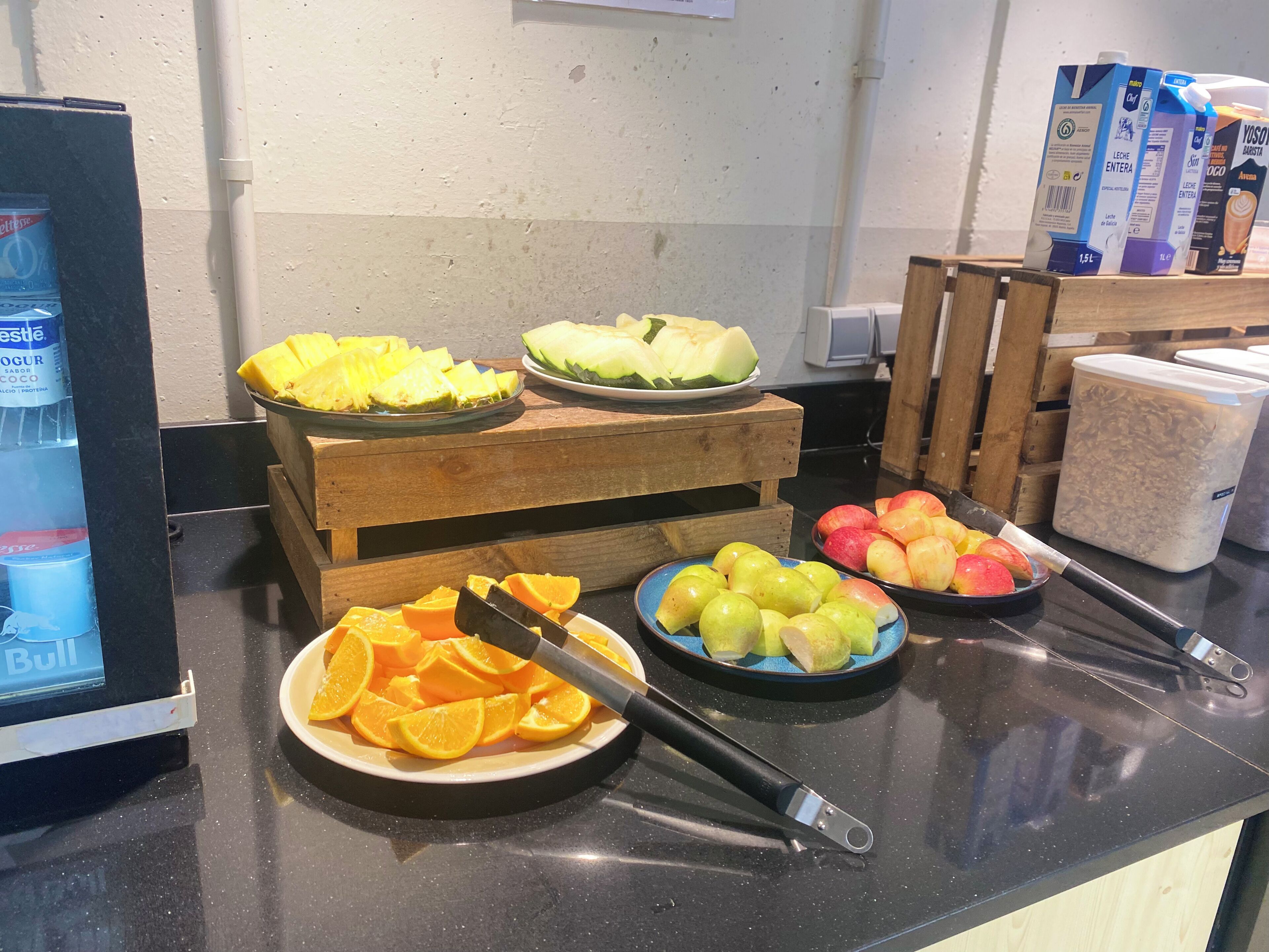 Mesa de buffet com diversas frutas e um dispensador de iogurte.