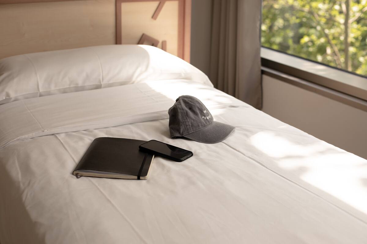A neatly made bed with a notebook, smartphone, and cap on it.