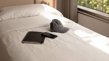 A neatly made bed with a notebook, smartphone, and cap on it.