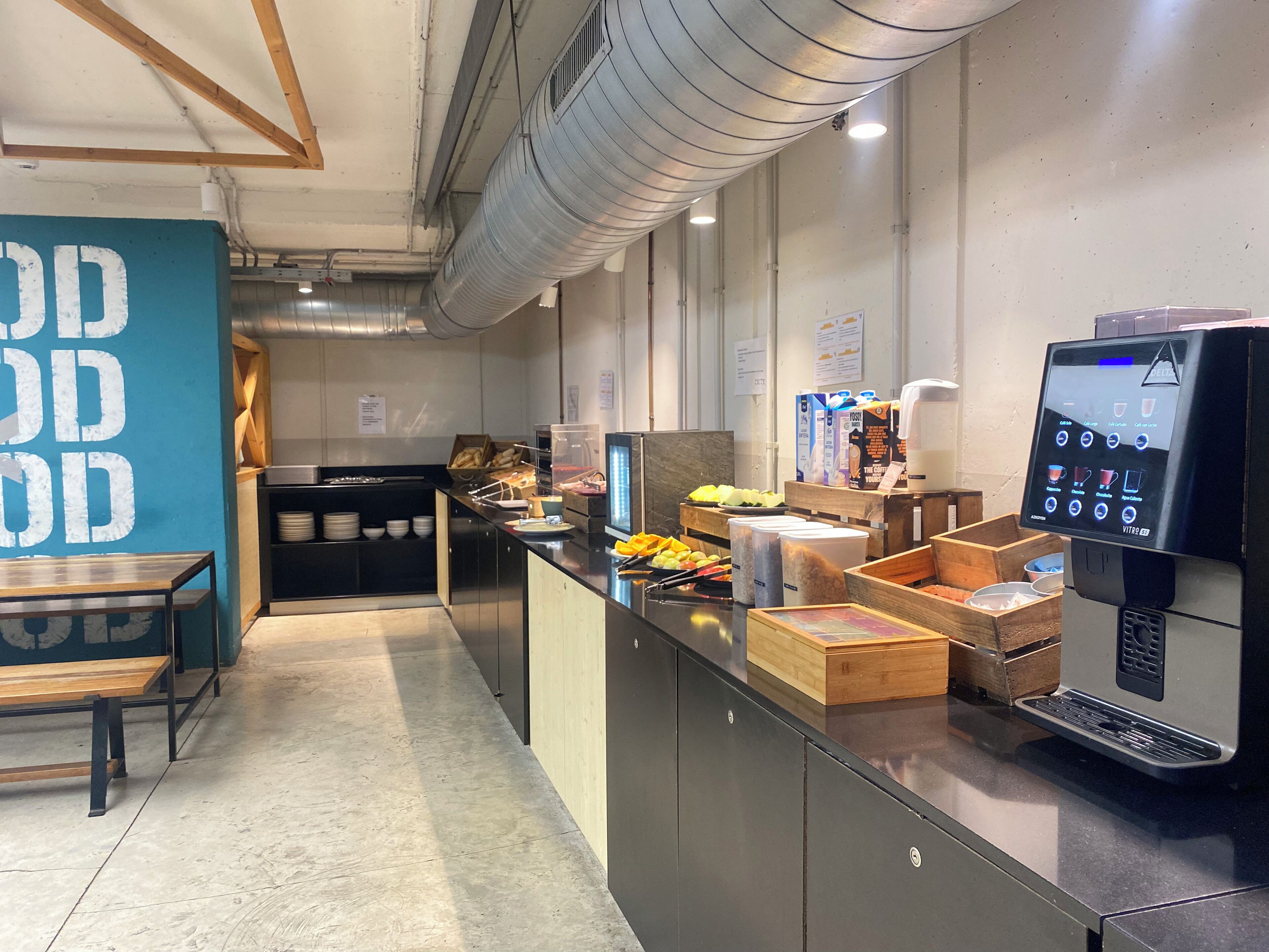 A modern kitchen area with a self-service station, including a coffee machine and various food items.