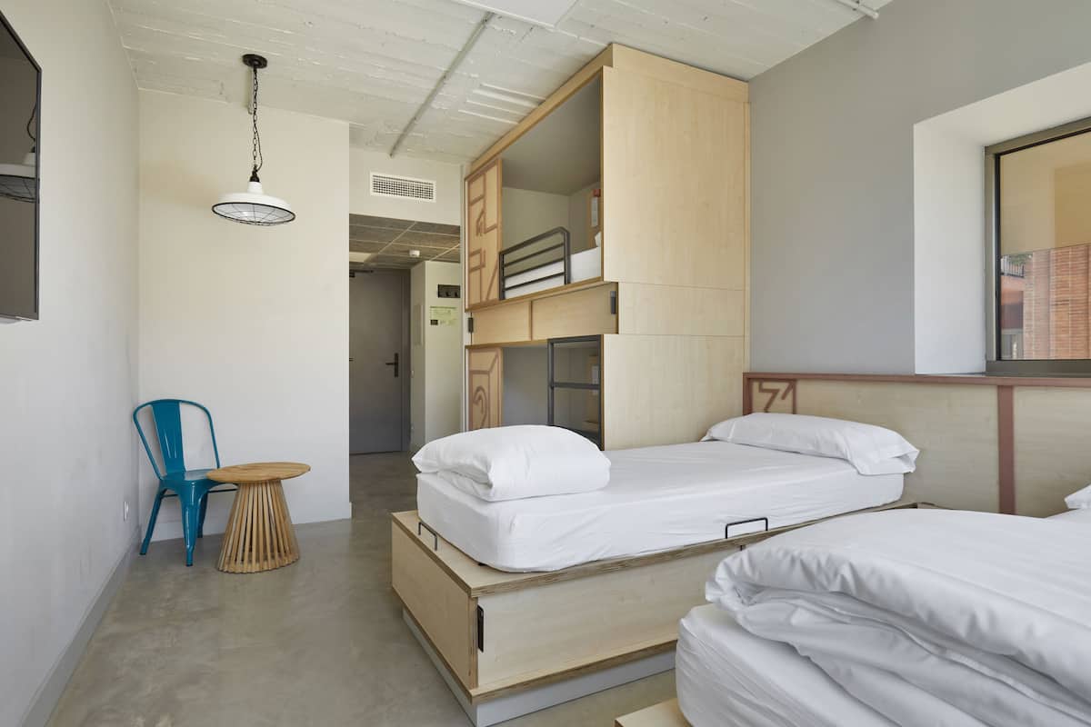 A compact bedroom with two beds, a small table, and a chair.