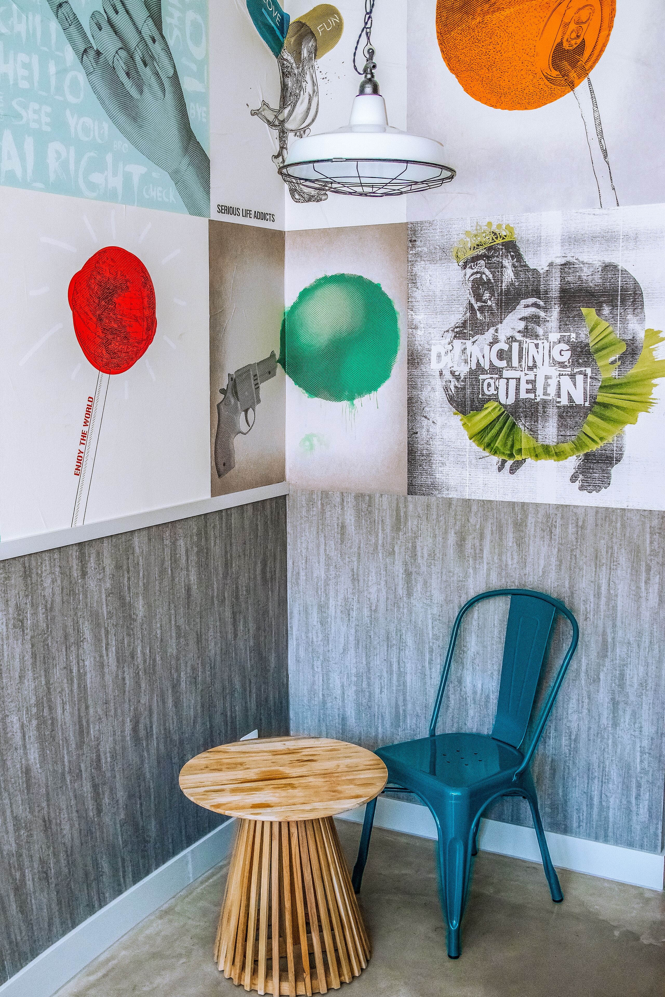 Een kamer met een smaragdgroene stoel, een houten tafel en een wand versierd met verschillende posters en een hanglamp.