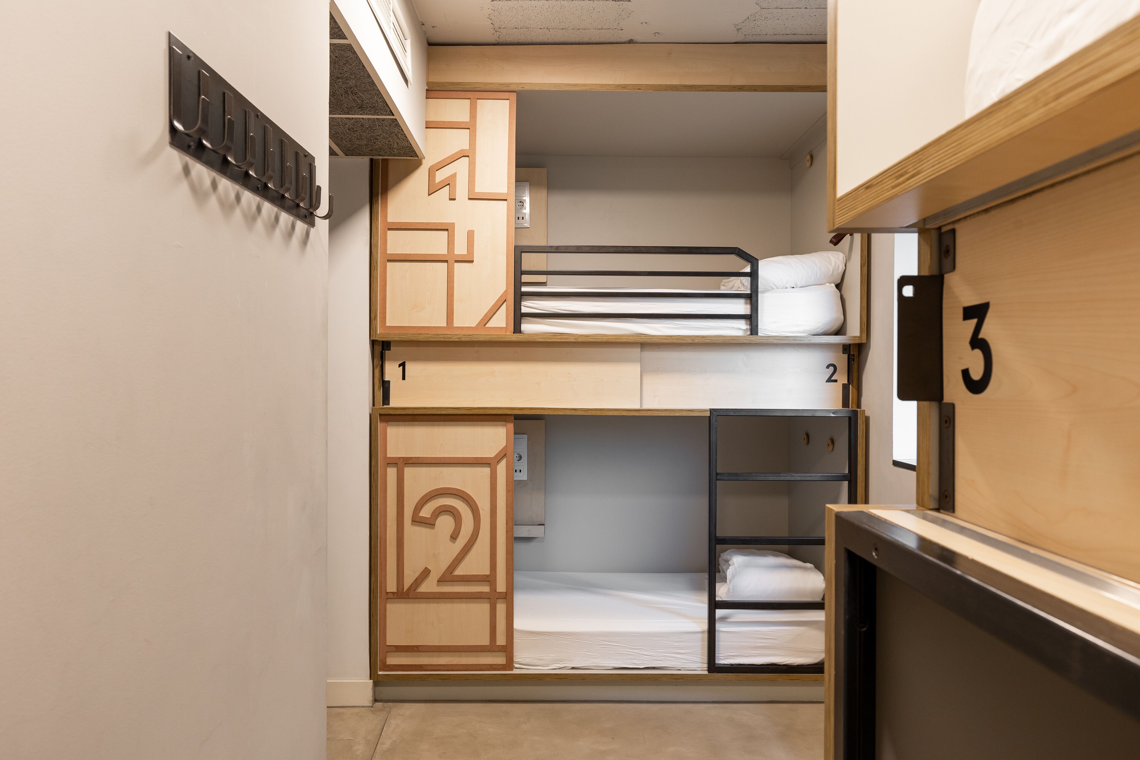 Habitación con literas, un armario de madera con el número 2 y un perchero metálico con ganchos.