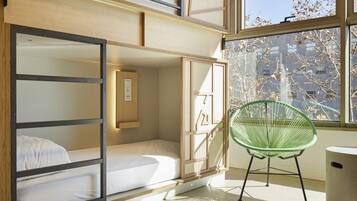 Une chambre avec un lit superposé, une chaise verte et une fenêtre donnant sur des arbres et des immeubles.