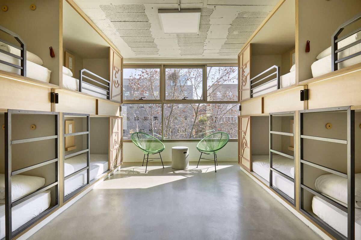 A dormitory room with bunk beds, a large window, and two green chairs.