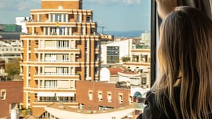Una persona mirando por la ventana un edificio de varios pisos con un diseño arquitectónico singular.
