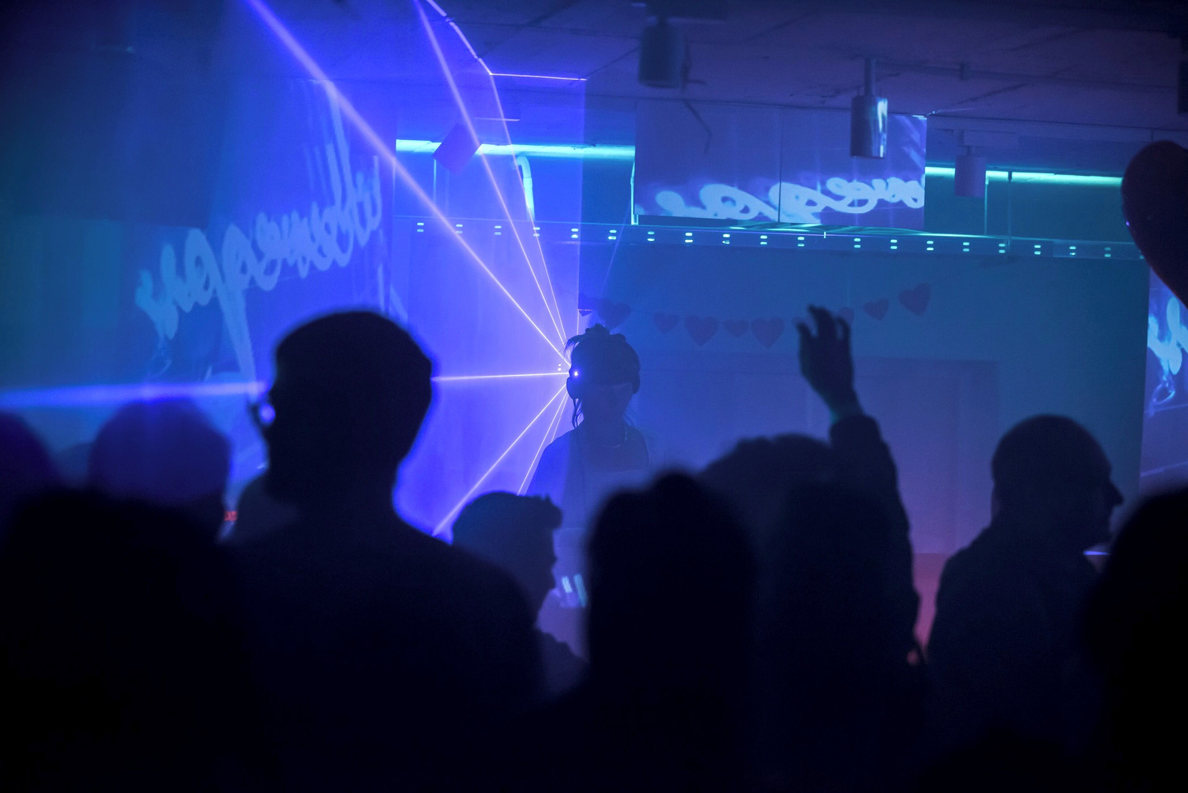 A dimly lit room with a large screen displaying text and a DJ booth.