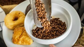 Une personne verse des grains de café dans un bol, avec des pâtisseries et des oranges en arrière-plan.