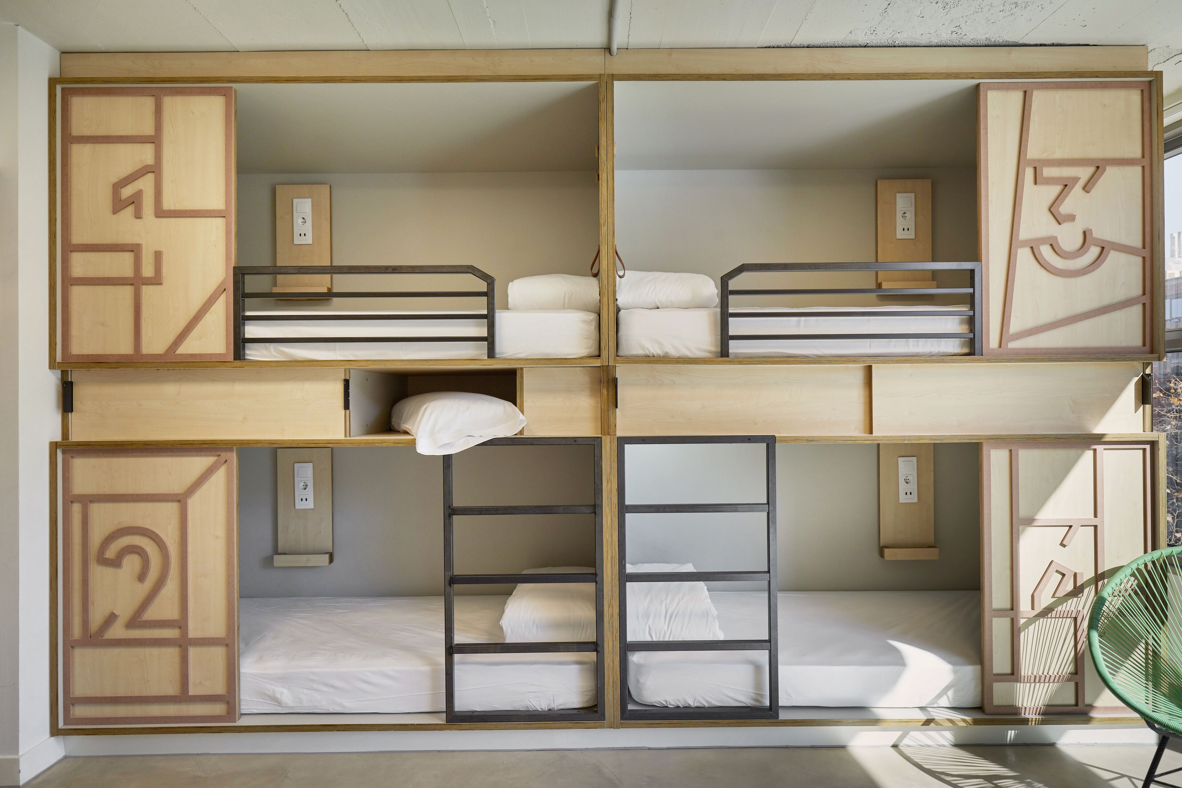 Quarto com beliches em vários níveis, separados por divisórias de madeira, cada uma com um número indicando a posição da cama.