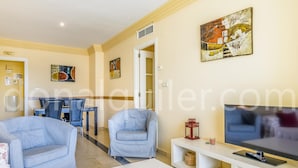 A living room with a TV, sofa, and chairs. There is a dining area with a table and chairs in the background. - Magnifico apartamento en Marbella (Marbella)