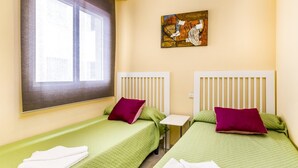 A hotel room with two single beds, each with a green bedspread and a white headboard. There is a painting on the wall above the beds, a window with a blind, and a small table between the beds. - Magnifico apartamento en Marbella (Marbella)