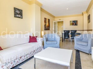 Un salon avec un canapé blanc, deux fauteuils, une table basse et un coin repas comprenant une table et des chaises.