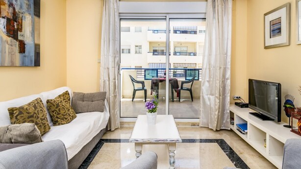 Un salon comprenant un canapé, une table basse, un téléviseur et un balcon offrant une vue sur les immebles.