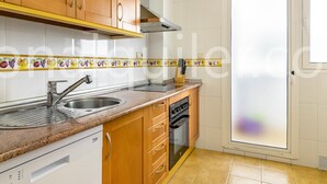 Cozinha com armários de madeira, pia de aço inoxidável, lava-louças e janela com vidro jateado.