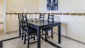 Un coin repas avec une table en bois foncé et quatre chaises, une œuvre d’art accrochée au mur et un sol carrelé de couleur claire.