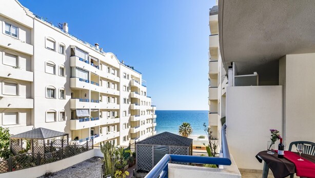 A hotel balcony with a view of the sea, a covered outdoor seating area, and a table with a red tablecloth.
