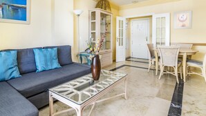 A living room with a sofa, a glass coffee table, and a dining area with wicker chairs.