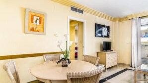 A dining area with a round table, wicker chairs, a potted plant, and artwork on the walls.
