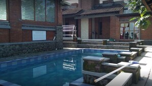 En swimmingpool med stenvægge og en bænk, omgivet af en bygning i murværk og sten.