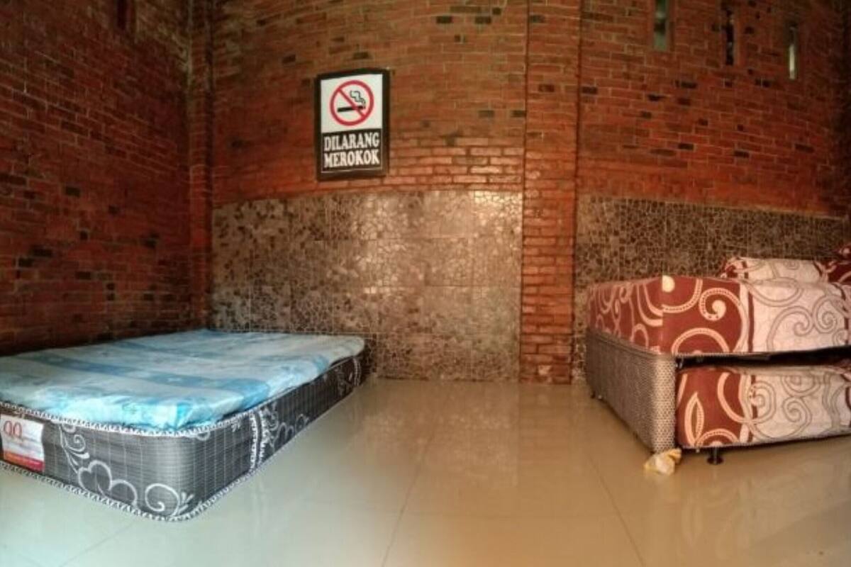 A room with a brick wall, a mattress on the floor, and a bed with patterned bedding.