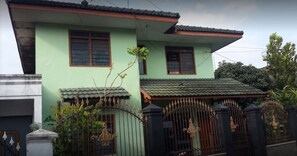 A two-story house with a green facade, a tiled roof, and a black iron gate with decorative elements.