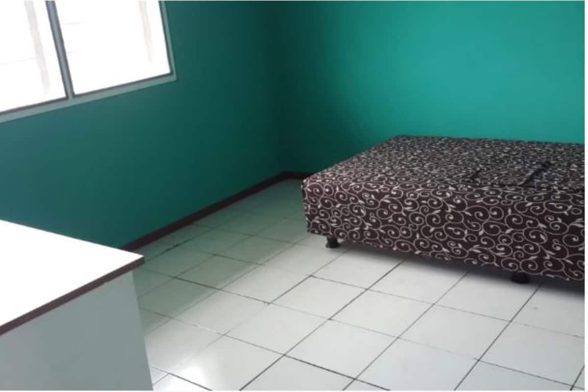 A room with teal walls, a patterned bed, a white desk, and a standing fan.