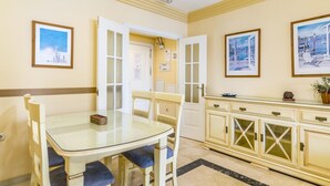 A dining area with a glass table and chairs, a cream-colored cabinet with glass doors, and two framed pictures on the wall. - Magnifico apartamento en Marbella con vistas al mar (Marbella)