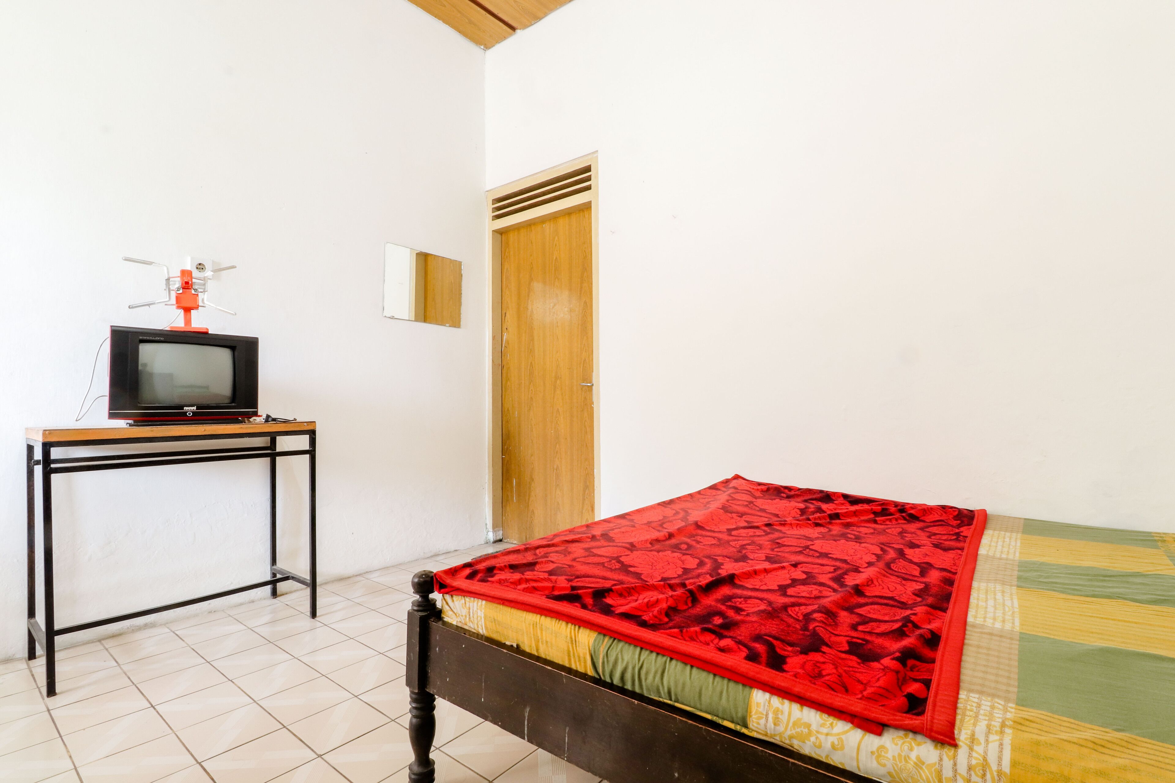 A room with a bed, a wooden door, a small table with a television, and a mirror on the wall.