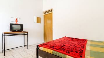A room with a bed, a wooden door, a small table with a television, and a mirror on the wall.