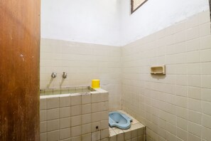 A small, tiled bathroom with a toilet, a sink with a yellow soap dispenser, and a water tank. - Wisma Joyo (Pakem)