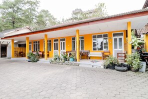 A yellow building with a covered patio area, outdoor seating, and potted plants. - Wisma Joyo (Pakem)