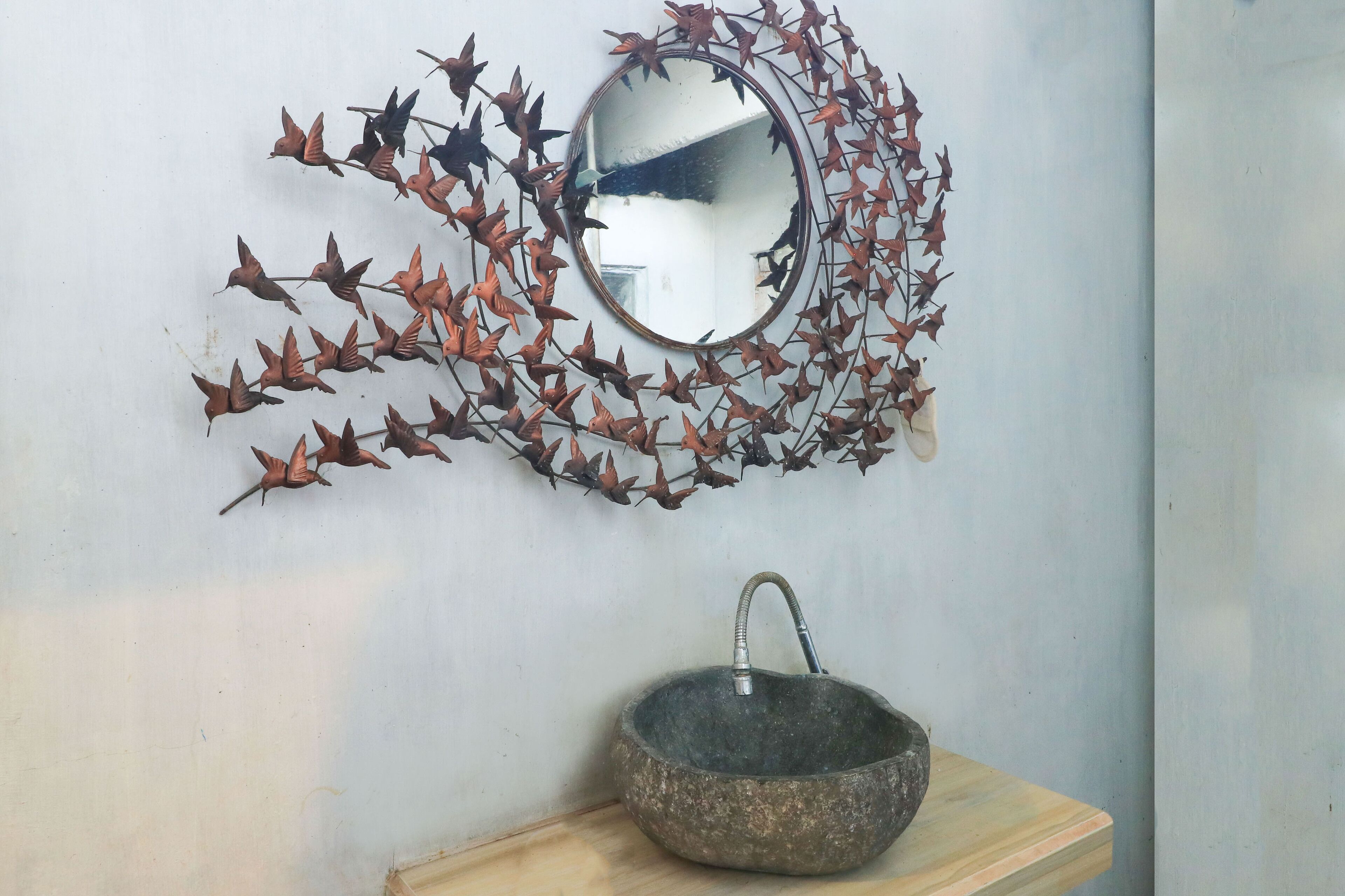 A wall-mounted mirror surrounded by a leaf-like metal decoration, with a stone basin below.