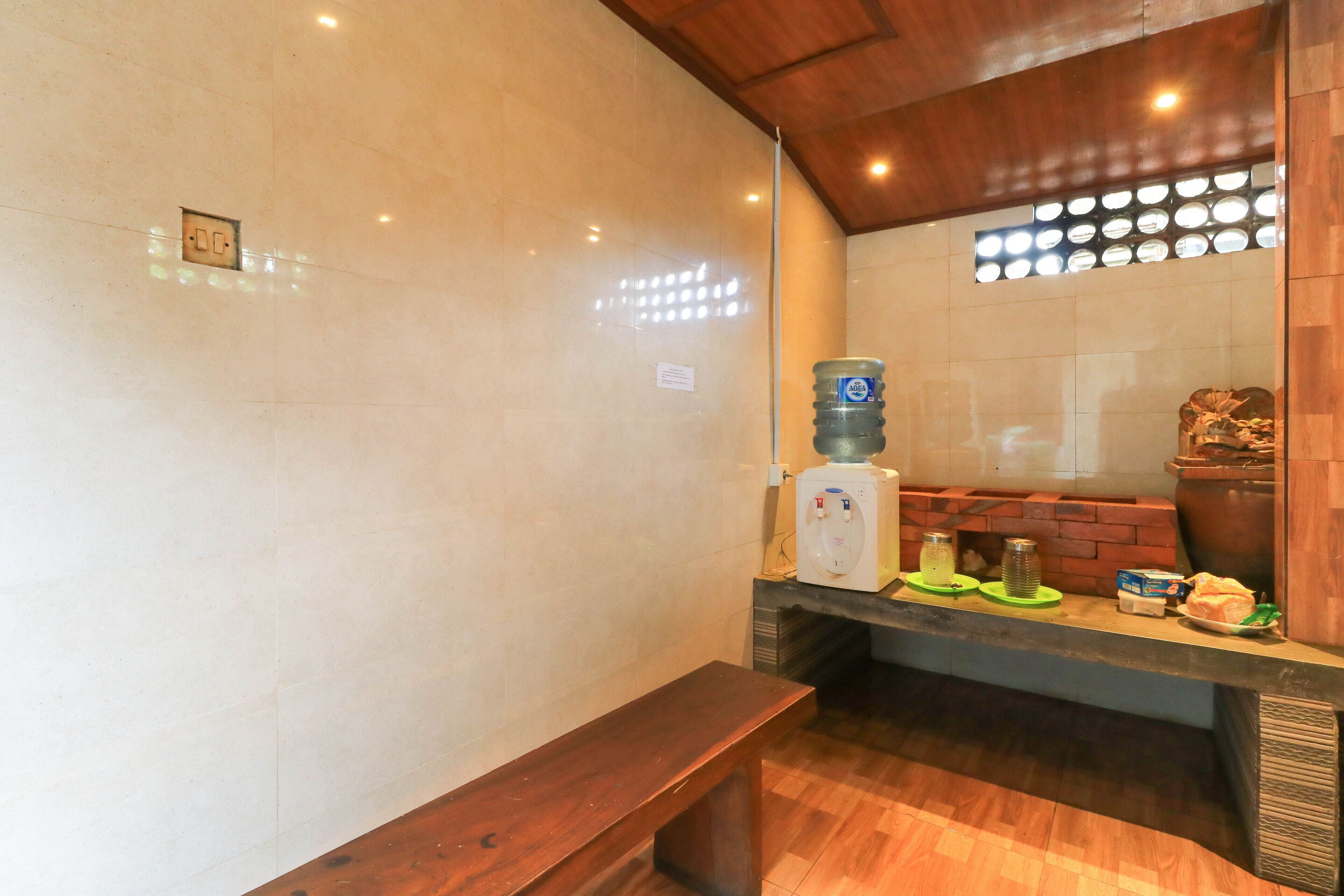 A bathroom with a wooden bench, a water dispenser, a sink, and a mirror with a circular light fixture above it.