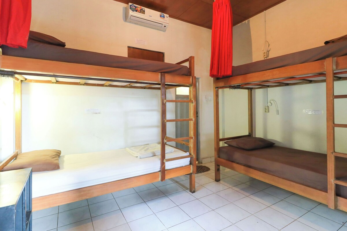 A dormitory room with bunk beds, a desk, and an air conditioning unit.