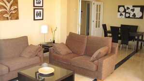 A living room with two sofas, a coffee table, a lamp, and a dining area with chairs and a table. - Frontal sea views penthouse (Marbella)