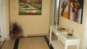 A hallway with a painting of a landscape, a potted plant, and a console table with decorative items. - Frontal sea views penthouse (Marbella)