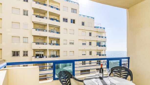 A balcony with a table and chairs, overlooking a building with multiple balconies and a view of the sea. - Magnifico apartamento en Marbella con vistas al mar (Marbella)