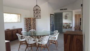 Comedor con mesa de vidrio, sillas blancas, aparador de madera y lámpara colgante.