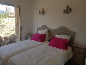 Double bed with two pillows, a nightstand, and a window offering a view of the surrounding landscape.