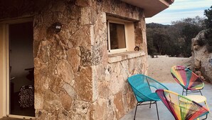 Un edificio de piedra con techo de tejas, una ventana pequeña y dos sillas coloridas afuera.