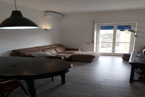 A living room with a brown sofa, a round dining table, and a pendant light.