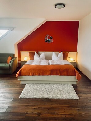 A bedroom with a bed, a sofa, a decorative wall piece, and a skylight.